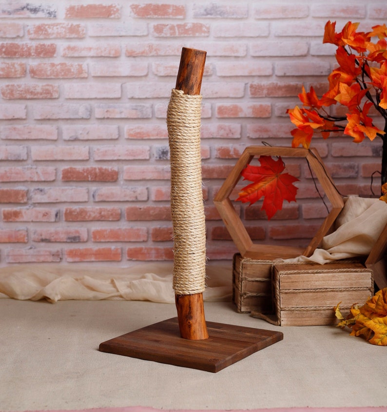 May include: A natural wood cat scratching post wrapped in sisal rope. The post is mounted on a square wooden base.