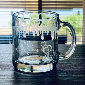 May include: A clear glass mug with a white etched design of honeycombs, dripping honey, and bees. The mug has a handle.