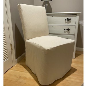 May include: A white linen slipcover chair with a simple, boxy design. The chair has a square seat and a high back.
