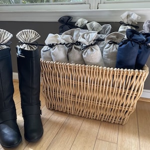 May include: A wicker basket filled with fabric sachets, some with a black and white striped pattern and others with a solid beige color. Two black leather boots with black and white striped fabric tops are in the foreground.