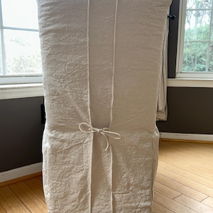 May include: A beige linen chair cover with a tie at the back.