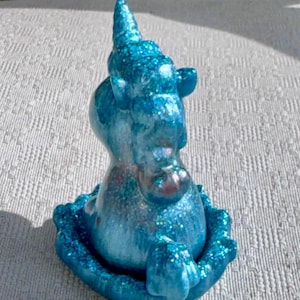 Pu&ograve; includere: Piccola statuetta di unicorno blu glitterato. L'unicorno ha un corno a spirale ed &egrave; seduto su una base decorativa. La statuetta &egrave; di una vibrante tonalit&agrave; di blu con accenti glitterati scintillanti, creando un'estetica stravagante e magica.