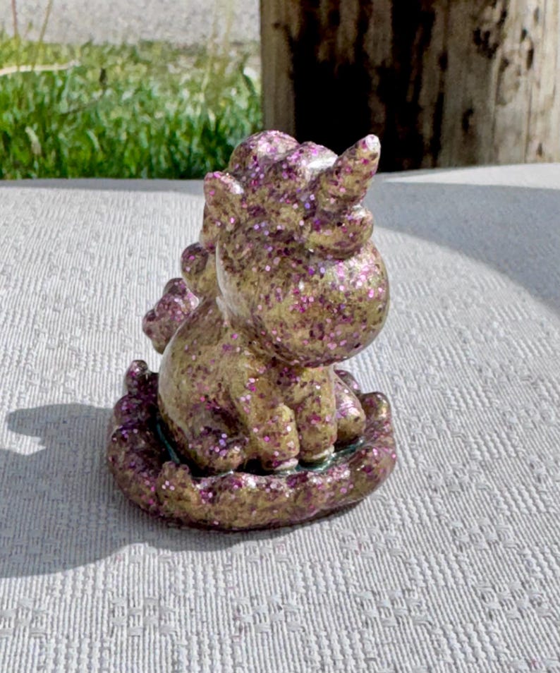 Pu&ograve; includere: Statuetta di unicorno dorata e glitterata con accenti di glitter viola. L'unicorno &egrave; seduto su una base decorativa e ha un singolo corno. &Egrave; un oggetto decorativo stravagante.