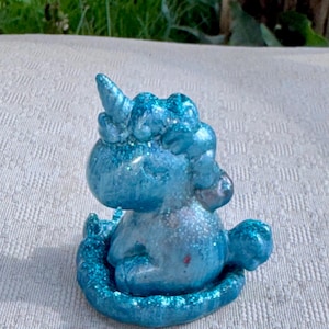 Pu&ograve; includere: Piccola statuina di unicorno blu glitterato. La creatura mitica &egrave; seduta, con il suo corno e la criniera dettagliati. La statuina &egrave; di un blu vibrante con accenti glitterati scintillanti e poggia su una base glitterata abbinata.