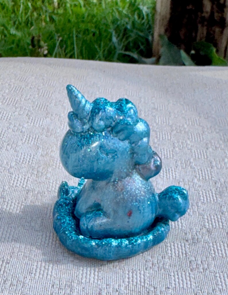 Pu&ograve; includere: Piccola statuina di unicorno blu glitterato. La creatura mitica &egrave; seduta, con il suo corno e la criniera dettagliati. La statuina &egrave; di un blu vibrante con accenti glitterati scintillanti e poggia su una base glitterata abbinata.