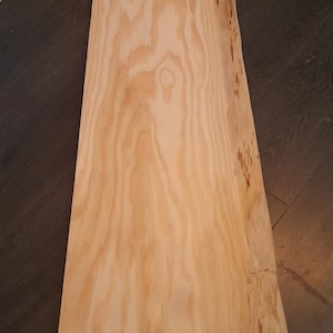 Peut inclure: Une planche de bois rectangulaire non finie, de couleur brun clair, avec des veines apparentes. La planche a une forme naturelle et irrégulière avec un bord légèrement incurvé. Le bois semble non traité, adapté à divers projets de menuiserie.