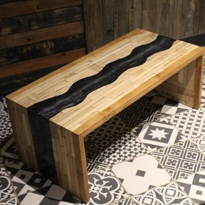 Peut inclure: Une table basse rectangulaire en bois avec un motif noir en forme de rivière au centre. La table est en bois clair et présente un design moderne et minimaliste. La table mesure environ 122 cm de long, 51 cm de large et 41 cm de haut.