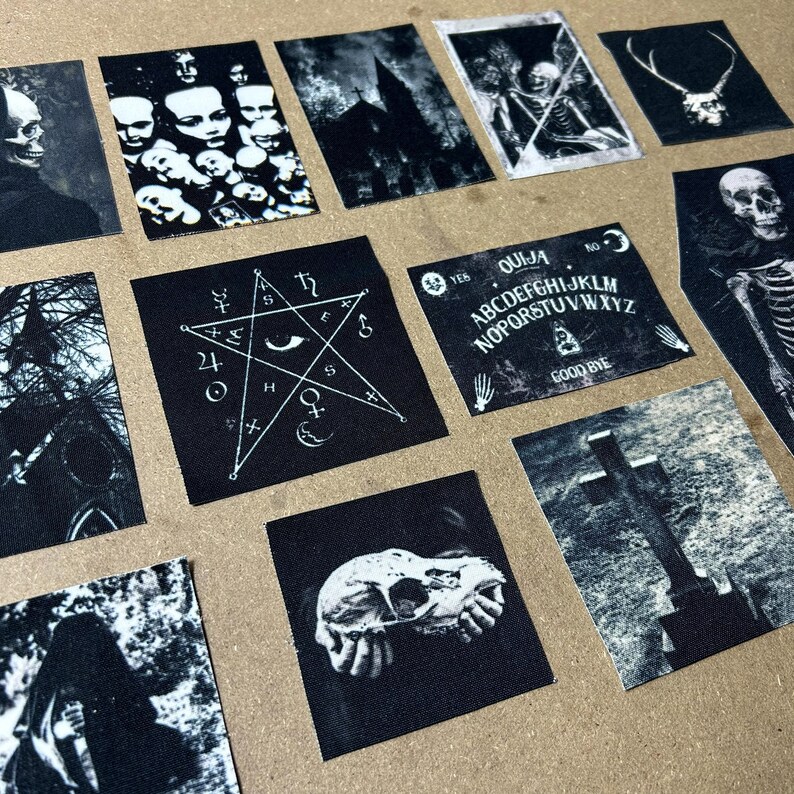 May include: A selection of black and white gothic patches. The patches depict skulls, a pentagram, a Ouija board with the text "QUIJA", and other dark imagery. The patches are displayed on a brown surface.