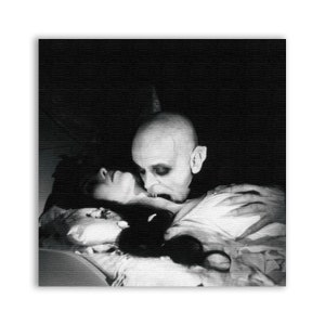 May include: A black and white photograph of a vampire biting a woman's neck. The vampire is pale and has sharp teeth. The woman is lying on a bed with her eyes closed.