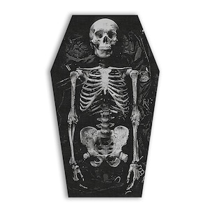 May include: A black and white image of a skeleton in a coffin. The skeleton is lying on its back with its arms crossed over its chest. The coffin is closed and has a black lining.