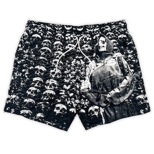 Puede incluir: Pantalones cortos de baño negros con cordón blanco. Los pantalones cortos están cubiertos con un patrón de calaveras blancas. Una figura de la Parca está impresa en la pierna derecha, sosteniendo una guadaña.