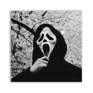 Peut inclure: Une personne portant un sweat-shirt à capuche noir et un masque de fantôme en plastique blanc avec une bouche grande ouverte et de grands yeux. Le masque est tenu devant le visage de la personne avec une main.