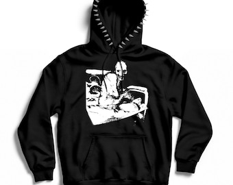 May include: A black hooded sweatshirt featuring a row of silver-toned metal spikes along the edge of the hood. The center of the chest displays a high-contrast white graphic print of a seated figure with a textured, sketch-like appearance.