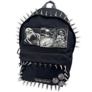 May include: Black backpack with silver spikes around the edges and on the front. The backpack features three black and white patches with gothic imagery. The bottom of the backpack has the text "TEMPER CRYPT" and three round pins.
