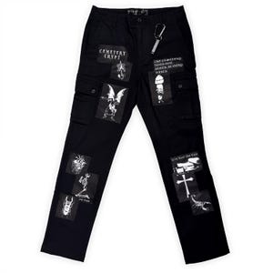 May include: Black cargo pants with multiple patches featuring gothic and punk-inspired imagery. Patches include skeletons, bats, and text like "Cemetery Crypt" and "Live Fast Die Fast." A silver carabiner clip hangs from the belt loop.