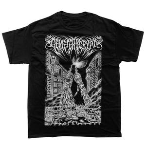 Può includere: T-shirt nero con grafica bianca dettagliata. Il design presenta una figura con cappotto lungo e cappello a cilindro in una strada cittadina, con la scritta "CEMETERY CRYPT" sopra. La scena è cupa e gotica.