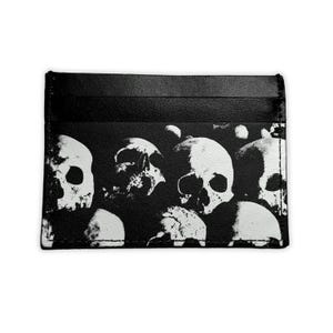 Può includere: Portacarte nero con stampa di teschi bianchi. Il portacarte ha più fessure ed è realizzato in un materiale liscio. Il design del teschio è un motivo ripetuto di teschi.