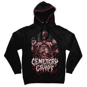 May include: A black hooded sweatshirt featuring a graphic of a decaying figure with exposed ribs and internal organs. The text "CEMETERY CRYPT" is printed in a distressed white font below the figure. The hood edge is lined with red spikes.
