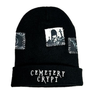 May include: Black beanie with a stitched-on patch featuring a graveyard scene and the text "CEMETERY CRYPT".