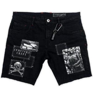 Op de afbeelding: Zwarte denim shorts met rafelige randen en patches. Patches tonen een schedel en gekruiste botten, een kerkhofscène en de tekst "CEMETERY CRYPT". Voorzien van een metalen karabijnhaak en rode stiksels.