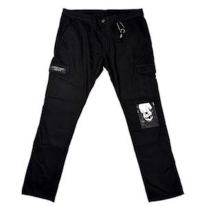 Op de afbeelding: Zwarte cargobroek met meerdere zakken en een kleine grafische patch op het rechterbeen. De broek heeft een rechte pijp en een sleutelhanger aan de riemlus. De tekst "CEMETERY CRYPS" is zichtbaar op een zak.