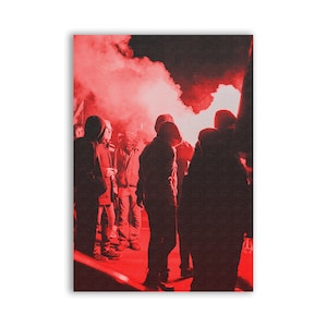 May include: A red-toned photograph depicts a crowd of people, silhouetted against a backdrop of red smoke. The individuals are wearing hooded jackets and standing close together. The scene is illuminated by a bright red light.