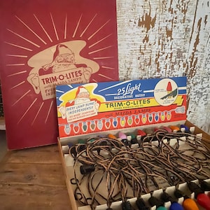 May include: A vintage Trim-O-Lites 25-light decorative outfit box featuring a Santa Claus illustration. The set includes a string of multi-colored light bulbs with black sockets and brown twisted wire, housed in a cardboard box with red and blue text.