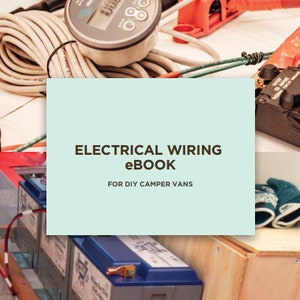 以下が含まれることがあります： DIYキャンピングカーの電気配線プロジェクトのクローズアップ。画像にはバッテリー、配線、デジタルメーターが表示されています。画像のテキストは「ELECTRICAL WIRING eBook FOR DIY CAMPER VANS」です。