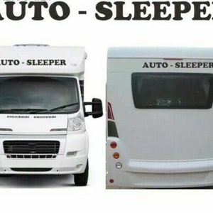 May include: White camper van with the words "AUTO -  SLEEPER" printed on the side. The van has a black grill and black headlights.