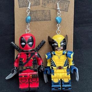Può includere: Orecchini fatti a mano con personaggi di Deadpool e Wolverine in stile Lego. Il personaggio di Deadpool è rosso e nero, con una spada. Il personaggio di Wolverine è giallo e blu, con artigli argentati. Gli orecchini hanno ganci argentati e perline blu.