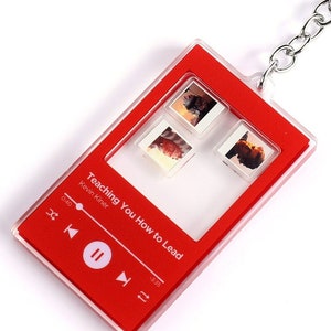 May include: Red acrylic keychain shaped like a music player with a clear window showing four small photos. The music player has the text "Teaching You How to Lead" and "Kevin Kinser" on it. The music player has play, pause, and skip buttons.