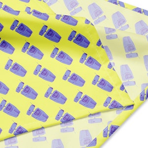 Op de afbeelding: Een gele stof met een herhaald patroon van blauwe en paarse retro-apparaten. De apparaten hebben een rechthoekige behuizing met een scherm en een antenne. De stof is gevouwen en toont het patroon aan beide zijden.