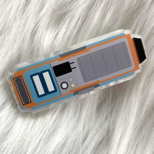 Op de afbeelding: Een blauw en oranje handapparaat met een grijs paneel en meerdere knoppen. Het apparaat heeft een zwarte antenne en een wit stroomkoord.