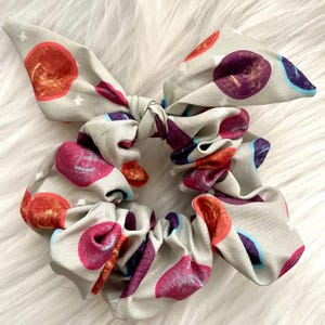 Op de afbeelding: Een grijze scrunchie met een kleurrijke abstracte print van cirkels. De scrunchie is gemaakt van zachte stof en is gebonden in een strik.