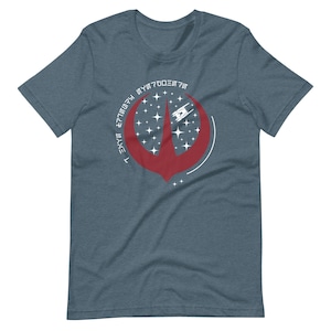 以下が含まれることがあります： 宇宙船と星が描かれた赤と白のグラフィックデザインが特徴の青いTシャツ。 デザインには様式化されたフォントのテキストが含まれています。 シャツは柔らかい素材で作られています。