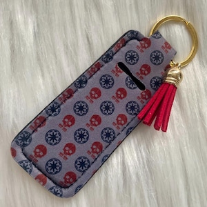 May include: A gray and blue key chain with a red tassel and a gold ring. The key chain has a repeating pattern of skulls and stars.