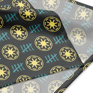 May include: Black fabric featuring a repeating pattern of yellow starburst circles and teal tally marks. The fabric is folded, showing a lighter grey underside. The design is consistent across the surface.