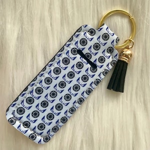 May include: A white and blue patterned fabric keychain with a gold key ring and a black tassel. The pattern features a repeating design of a black circle with a blue star inside.