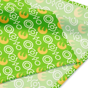 May include: Green fabric with a white and yellow repeating pattern of circles and a symbol. The fabric is folded over on itself.