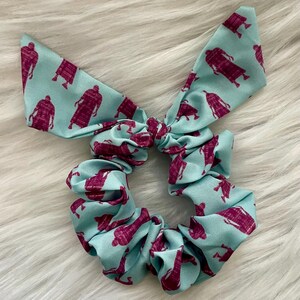 May include: A light blue scrunchie with a repeating pattern of burgundy figures. The scrunchie is tied in a bow.