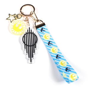 May include: A gold-toned keychain with multiple charms. Charms include a yellow star, a yellow circle with a symbol, and a clear, black-lined design. A blue and white striped lanyard with repeating yellow circle and black spaceship designs.