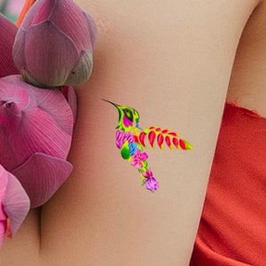 May include: A colorful hummingbird tattoo design with pink, yellow, green, and red flowers. The tattoo is on a person's arm.