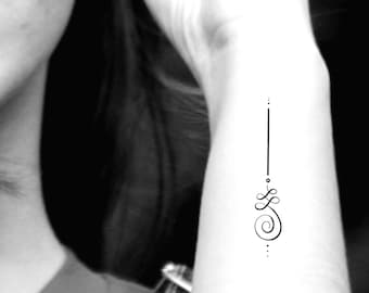 May include: A black and white image of a simple line art tattoo design on a person's wrist. The design features a vertical line with a spiral and two dots at the top and bottom.