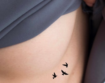 May include: A close-up of a person's side with a small tattoo of three black birds flying in a row.