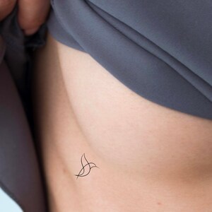 May include: A simple line drawing tattoo of a bird on a person's side.