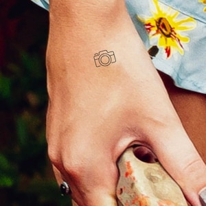 May include: A simple line drawing of a camera on a person's arm.