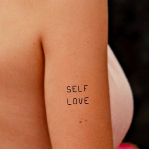 May include: A close-up of a person's arm with the words "SELF LOVE" written in black ink.