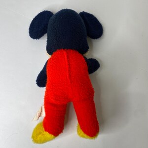 Puede incluir: Un juguete de peluche vintage de un personaje de dibujos animados, con una cabeza azul marino y orejas grandes, un cuerpo rojo y pies amarillos. El juguete est&aacute; sobre una superficie blanca. Un juguete cl&aacute;sico para ni&ntilde;os.