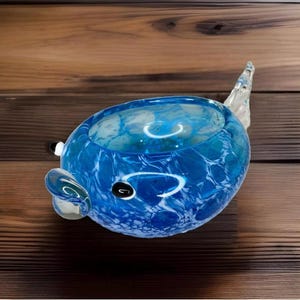 May include: A blue glass sculpture of a pufferfish with white marbling. The sculpture has a rounded body and a tail fin.
