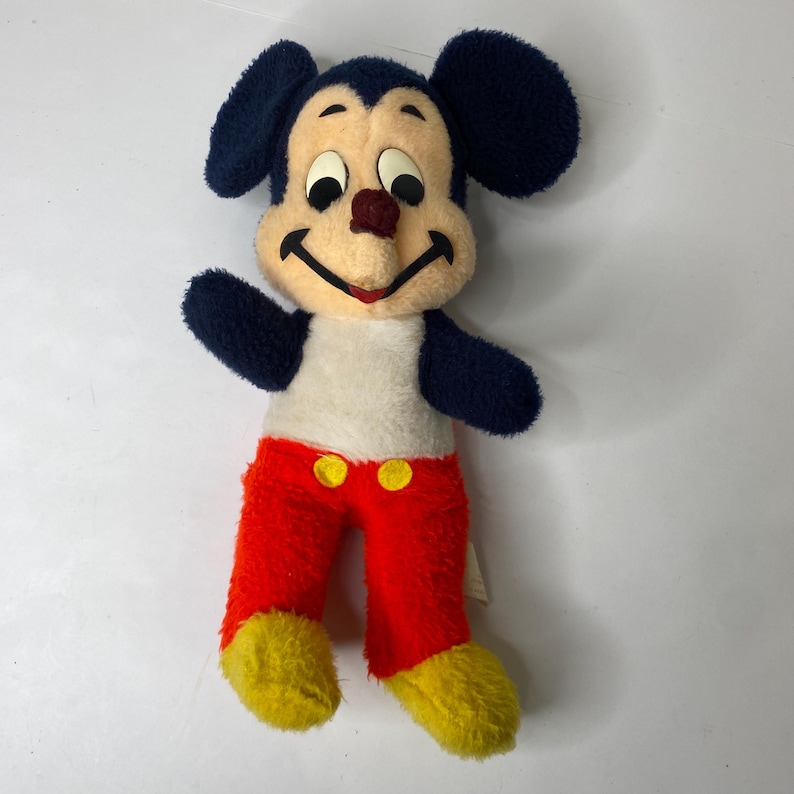 Puede incluir: Peluche vintage de Mickey Mouse. El peluche presenta una cara color crema, una cabeza y orejas azul oscuro y una nariz roja. Mickey lleva pantalones rojos con botones amarillos y pies amarillos. El juguete est&aacute; en buenas condiciones.